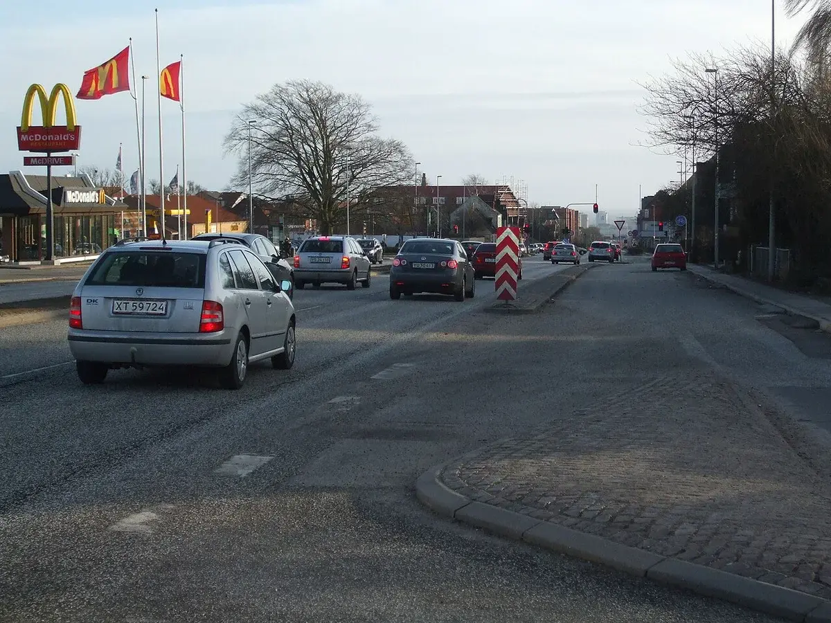 Cars driving along a wide urban road near a McDonald's.