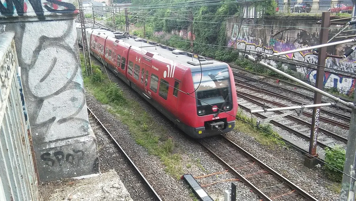 A red DSB train on tracks beside graffiti-covered railway walls.