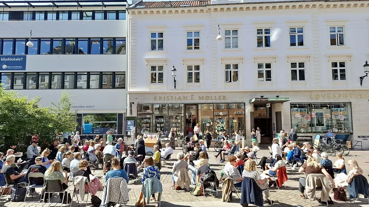 People seated outdoors at a literary event in a sunny city square in Aarhus