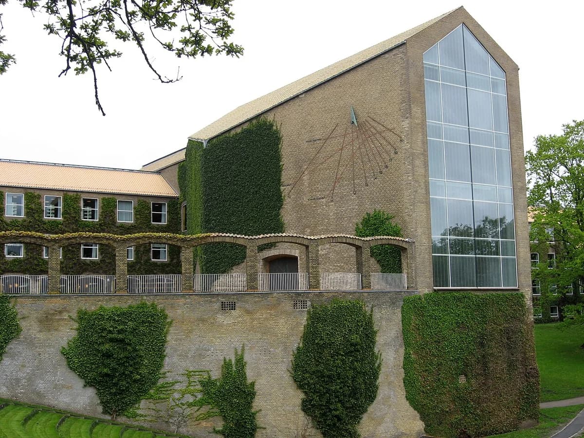 Back of Aarhus University’s main building with ivy-covered brick walls and a tall glass facade.