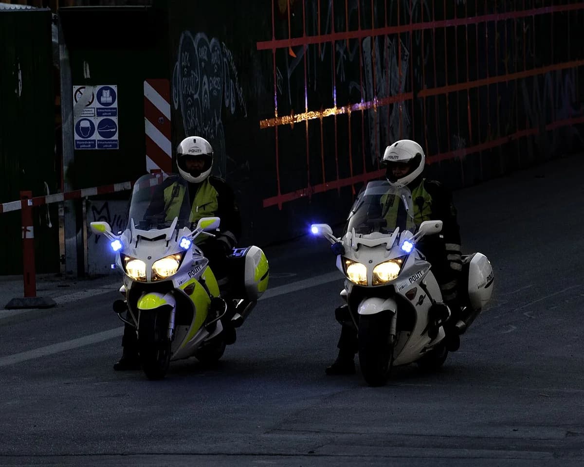 Two Danish police officers ride motorcycles with lights on at night.