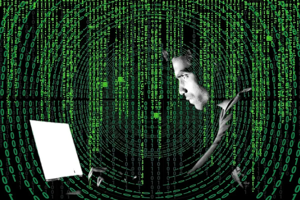 A man using a laptop surrounded by green binary code and digital rings.