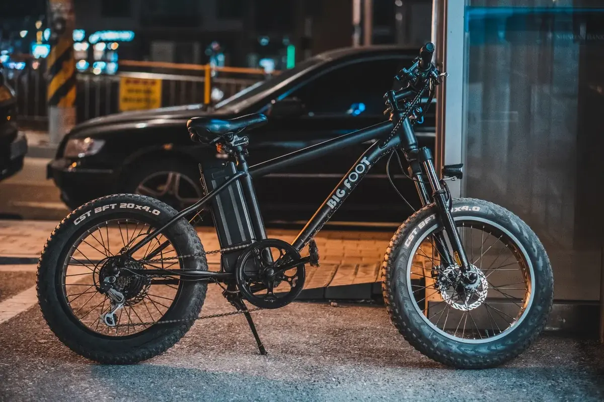 A black electric bike with fat tires parked on a sidewalk at night.