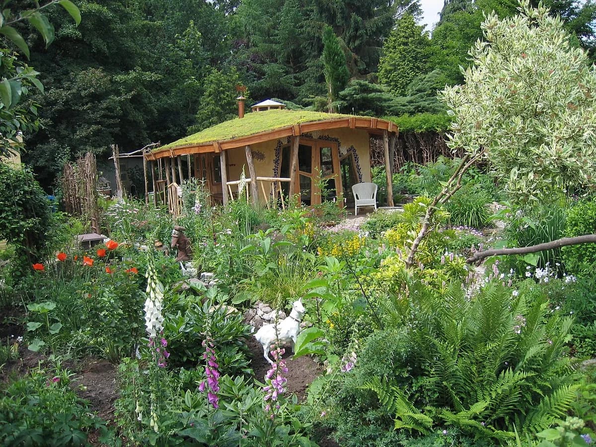 A small grass-roofed garden house in a lush garden.