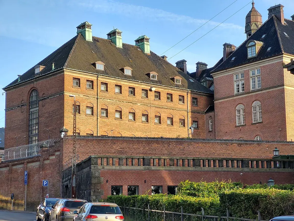 Historic red-brick prison building in Aarhus, Denmark, with barred windows and barbed wire
