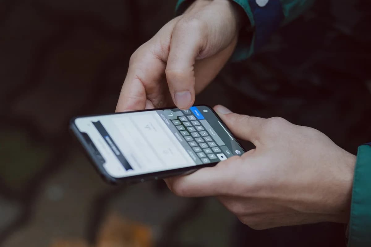 Hands typing a message on a smartphone outdoors.