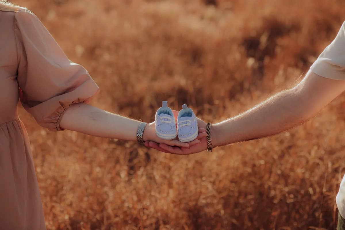 Two parents hold tiny blue baby shoes between them outdoors.