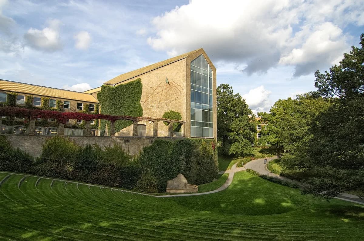 Exterior of the Aula building at Aarhus University with ivy-covered brick walls and a large glass facade.