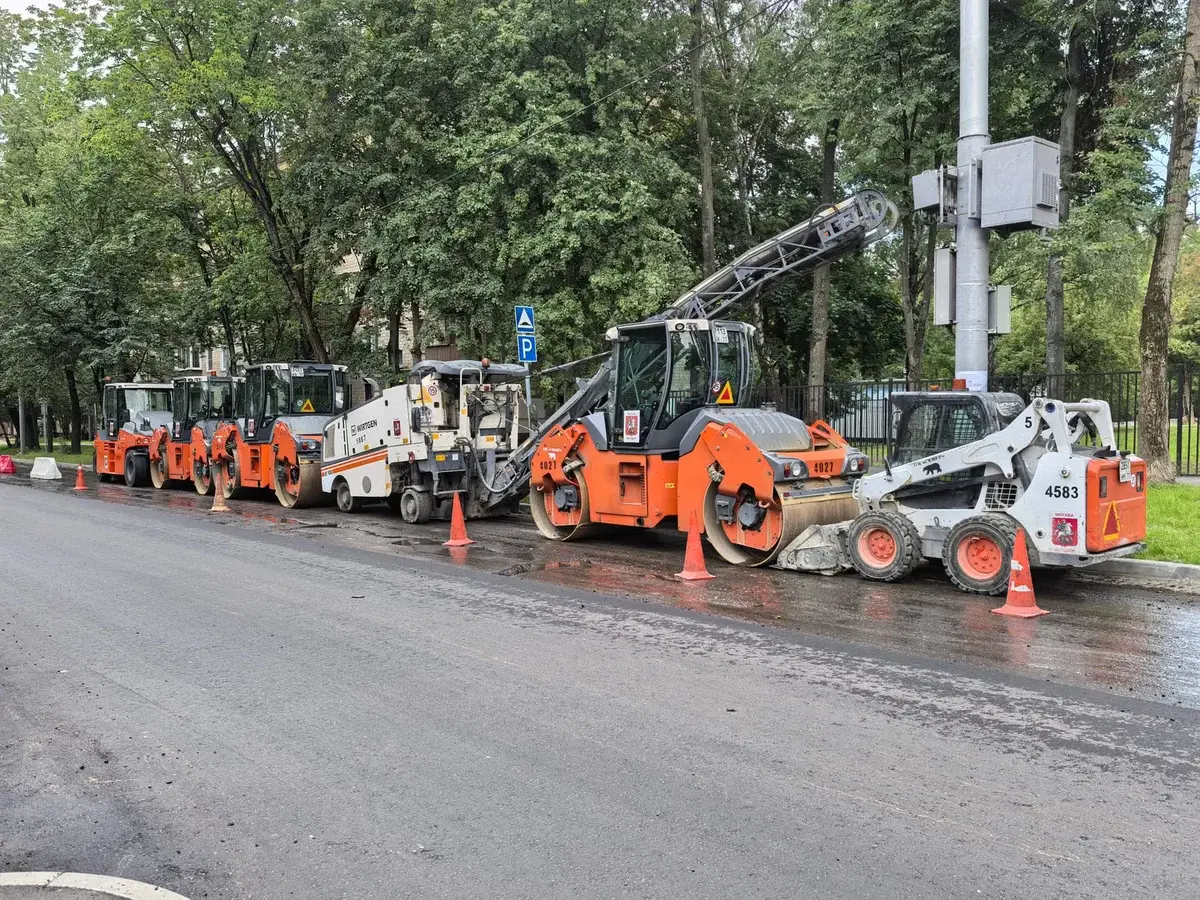 Road construction equipment lined up on a city street beside traffic cones.