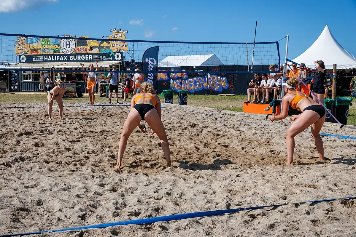 Women playing beach volleyball on a sandy court at a festival.