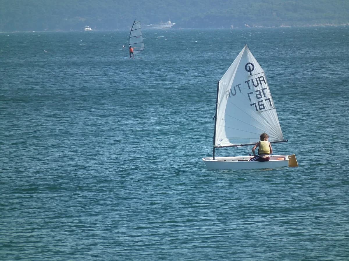 A small sailboat with a sailor on calm coastal water.