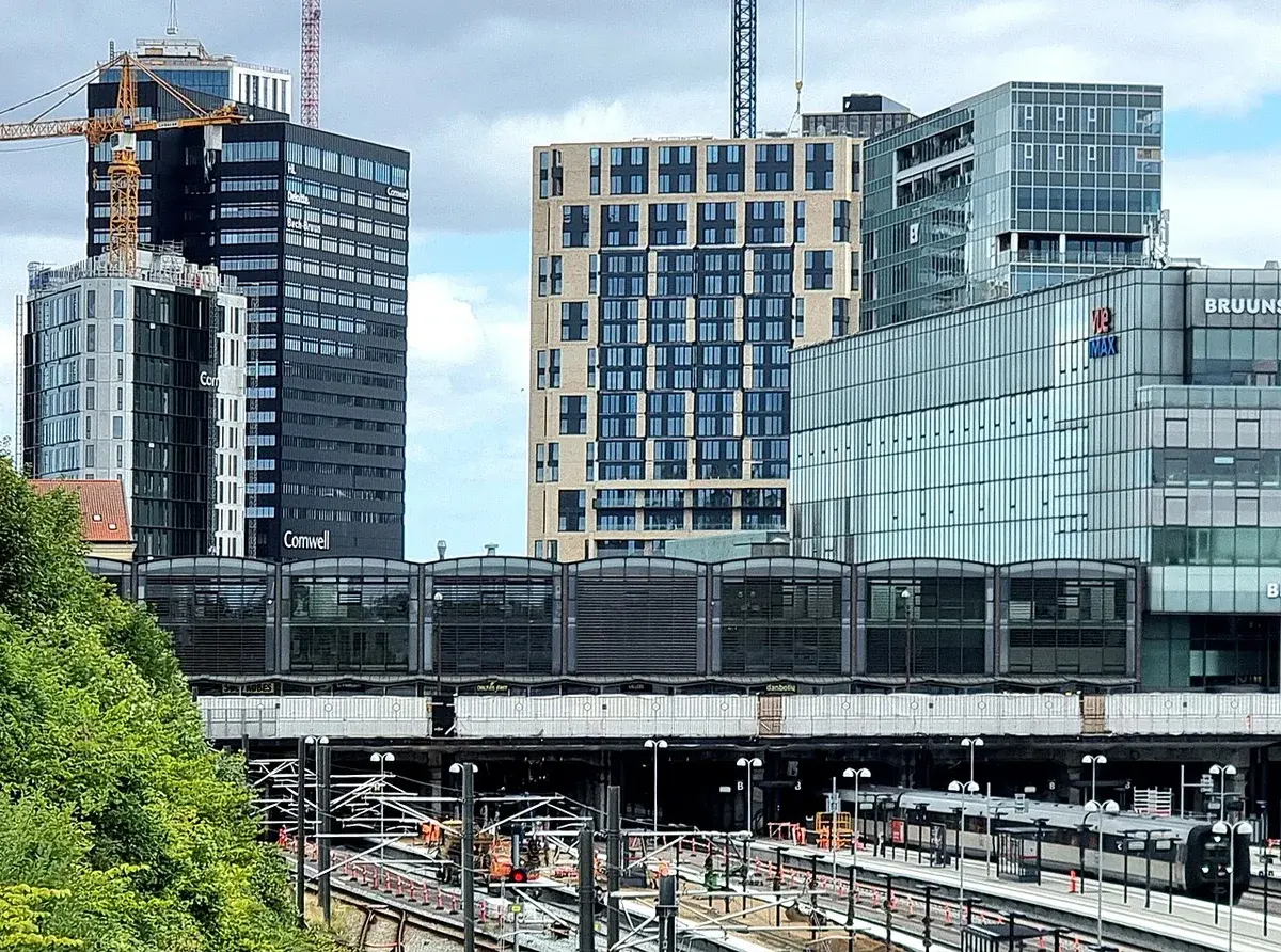 Modern skyline of Aarhus with high-rise buildings and cranes near a rail station.