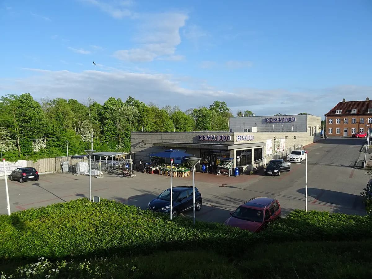 Rema 1000 supermarket with a parking lot and trees in the background.