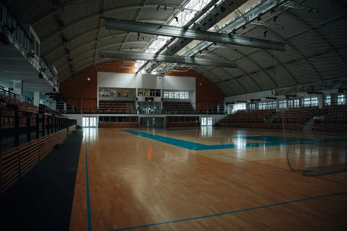 Empty indoor sports arena with hardwood floor and tiered seating.