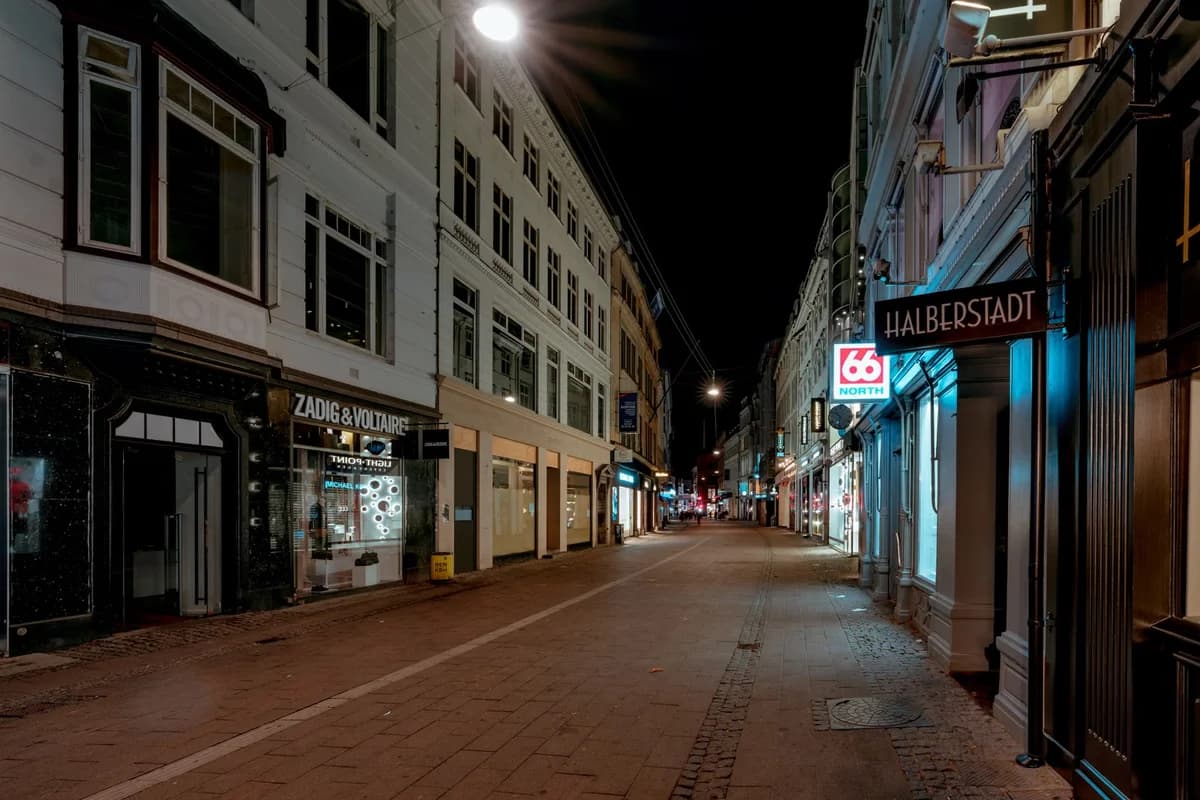 Empty Copenhagen street at night with lit shop windows and street lamps.