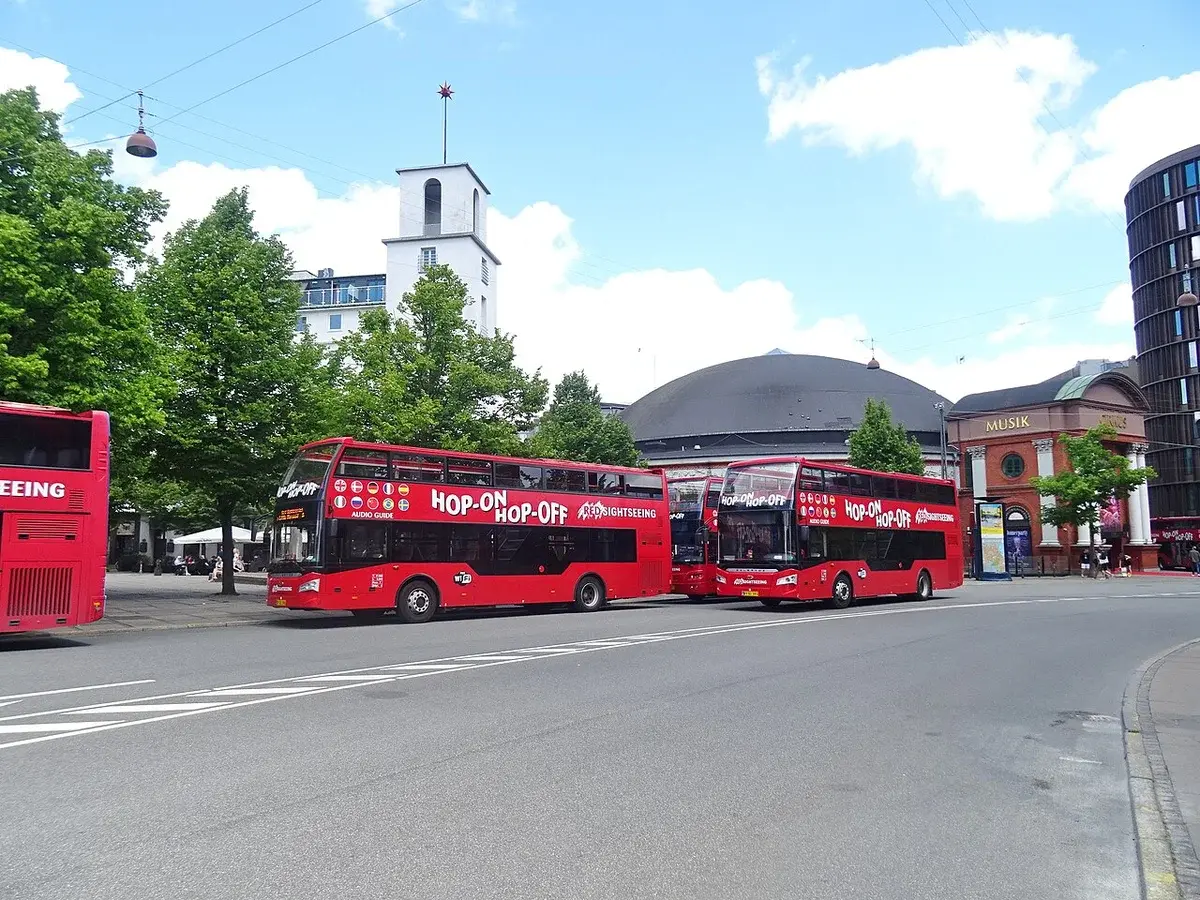 Two red sightseeing buses parked on a street in Copenhagen near the Cirkusbygningen.