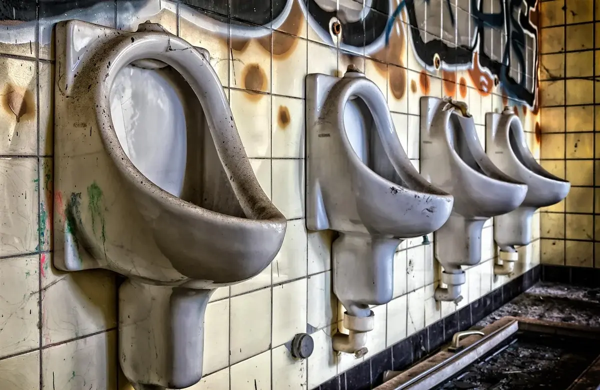 A row of dirty urinals in a neglected, graffiti-covered restroom.