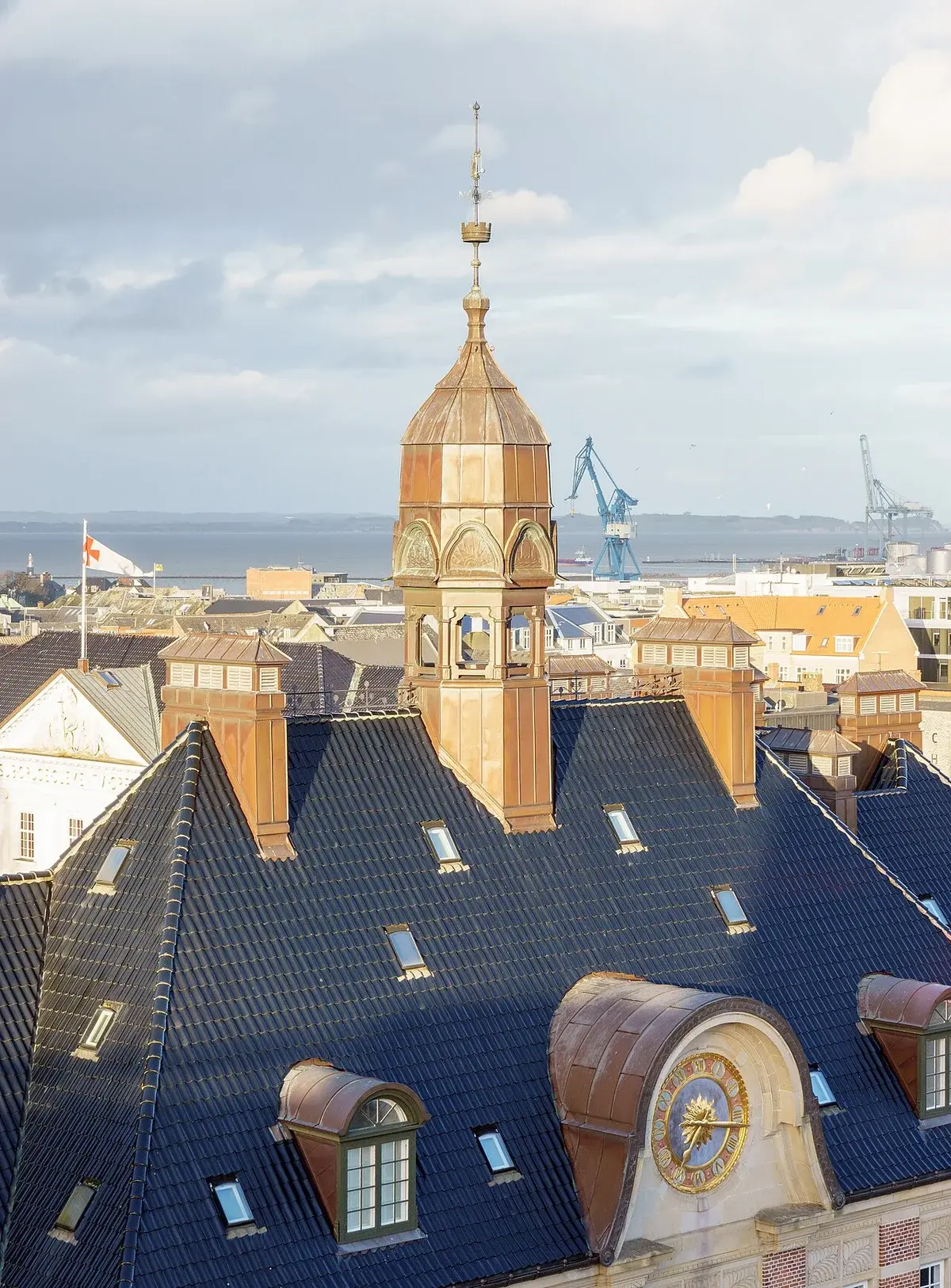 Roof and tower of Aarhus City Hall with the harbor in the background.