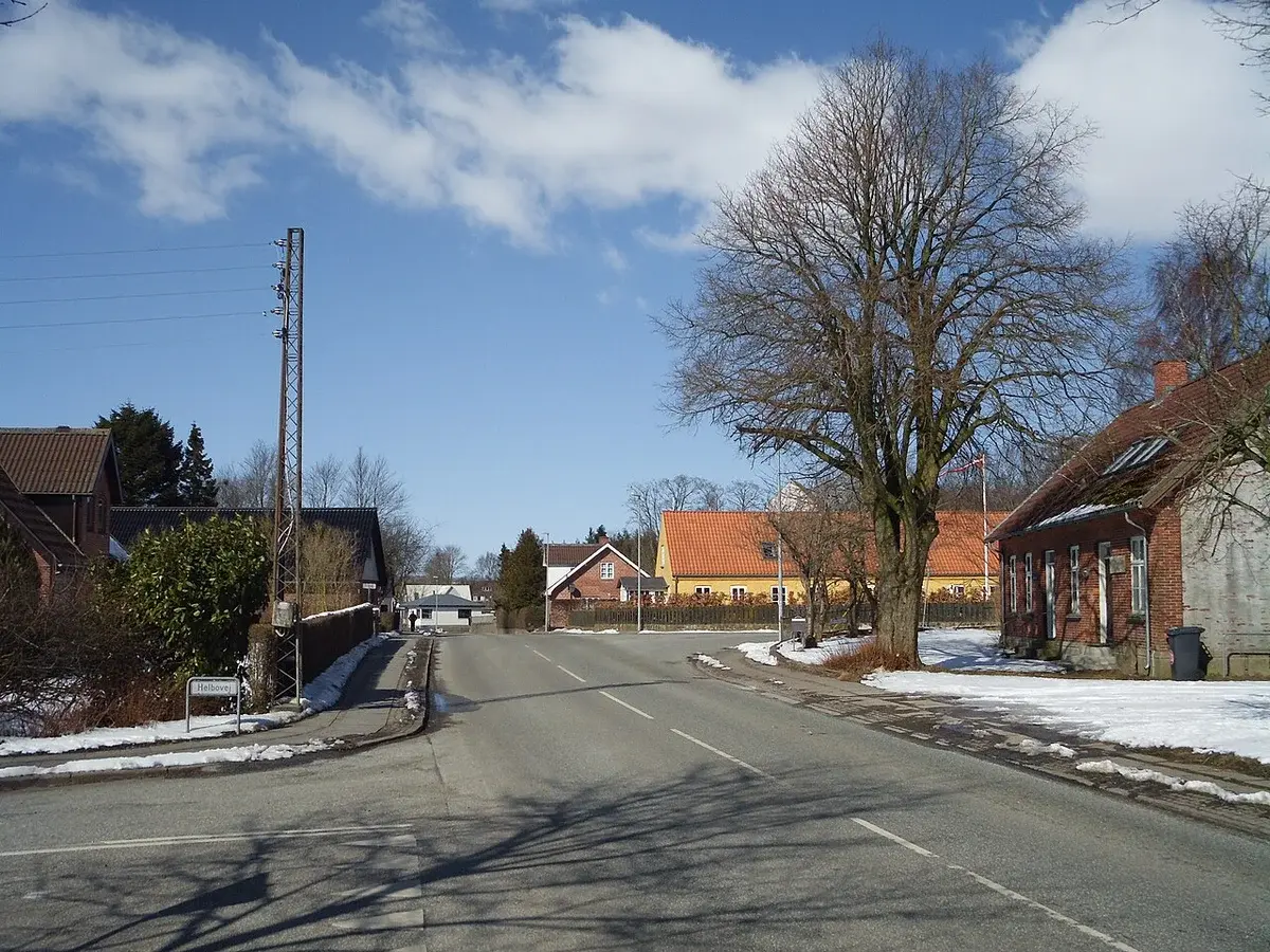 A quiet village road intersection with houses, bare trees, and patches of snow.