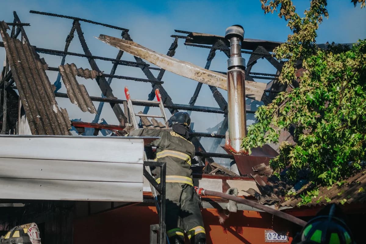 Firefighter removing debris from a burned roof after a house fire.