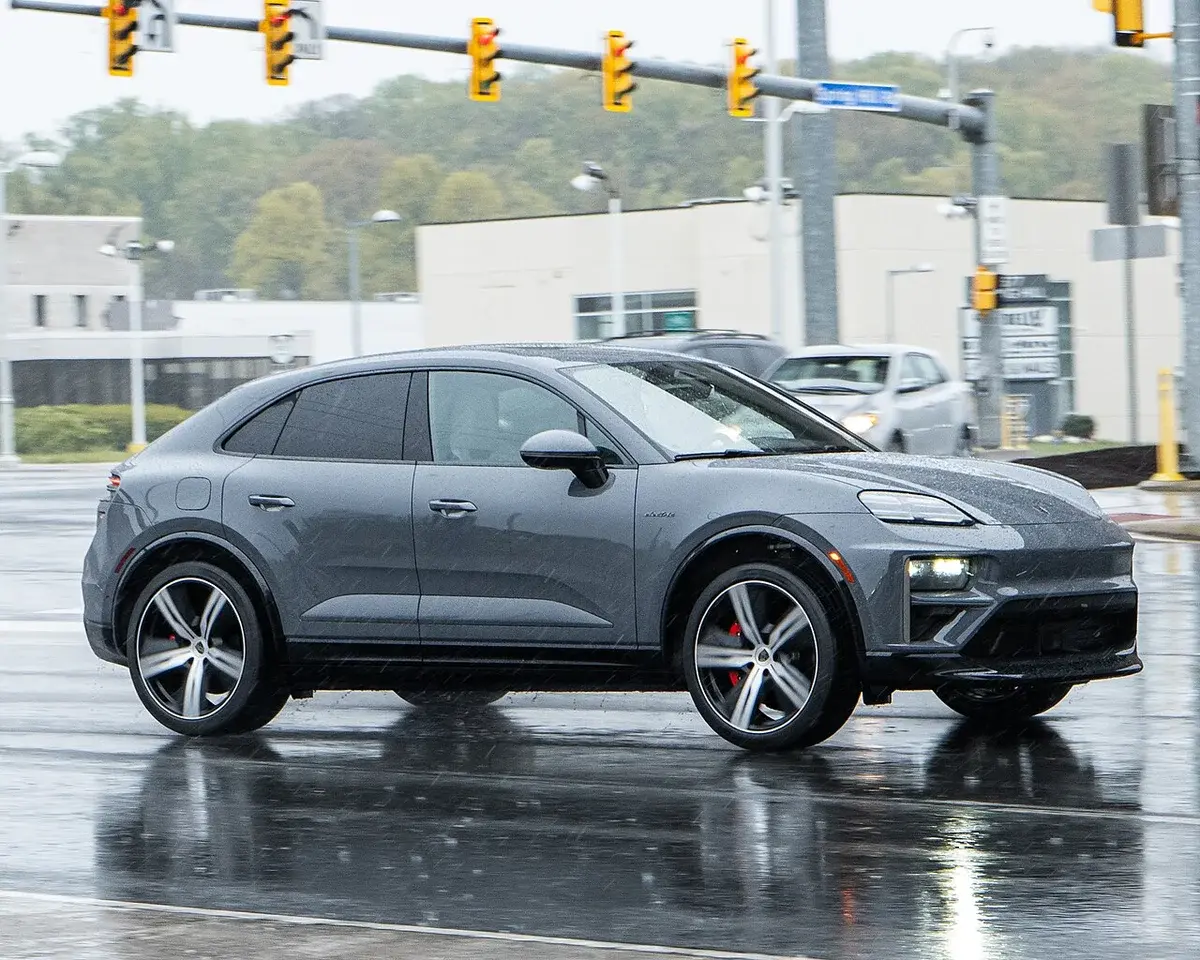 Gray Porsche Macan EV driving on wet urban street