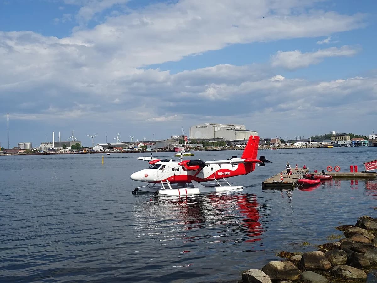 A red and white seaplane floating in Copenhagen Harbour near a dock.